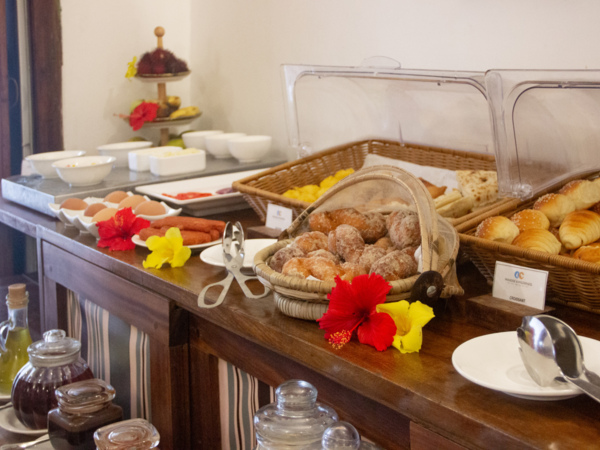 Breakfast buffet with assorted fresh pastries, croissants, boiled eggs, jams, and tropical flowers on a wooden counter