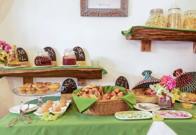 Breakfast buffet with fresh muffins, boiled eggs, assorted breads, jam, olive oil, nuts, and fresh vegetables on green table linens