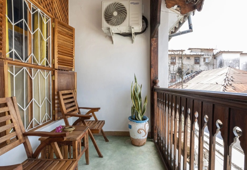 Cozy wooden balcony with two chairs, small table, potted plant, and view of rustic rooftops in a traditional setting