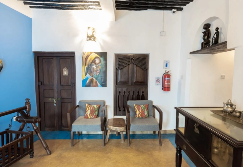 Cozy hotel seating area with two armchairs and colorful pillows, rustic wooden doors, a vibrant blue accent wall, and cultural decor.