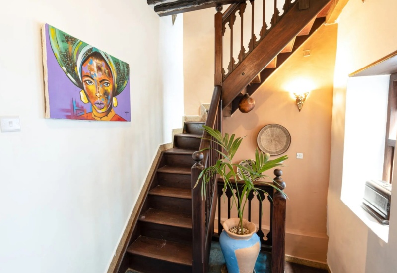 Cozy wooden staircase with carved railing, vibrant wall art, potted plant, and warm lighting in a charming hotel interior