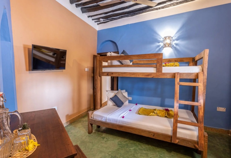 Cozy room with wooden bunk beds, colorful blue and peach walls, ceiling fan, flat-screen TV, and wooden dresser with water jug and glasses