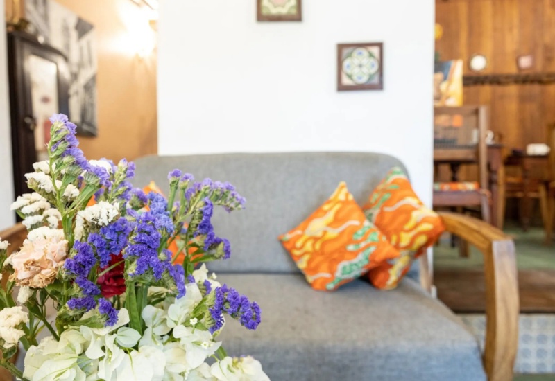 Cozy seating area with gray cushioned sofa, vibrant orange patterned pillows, and fresh purple and white floral arrangement