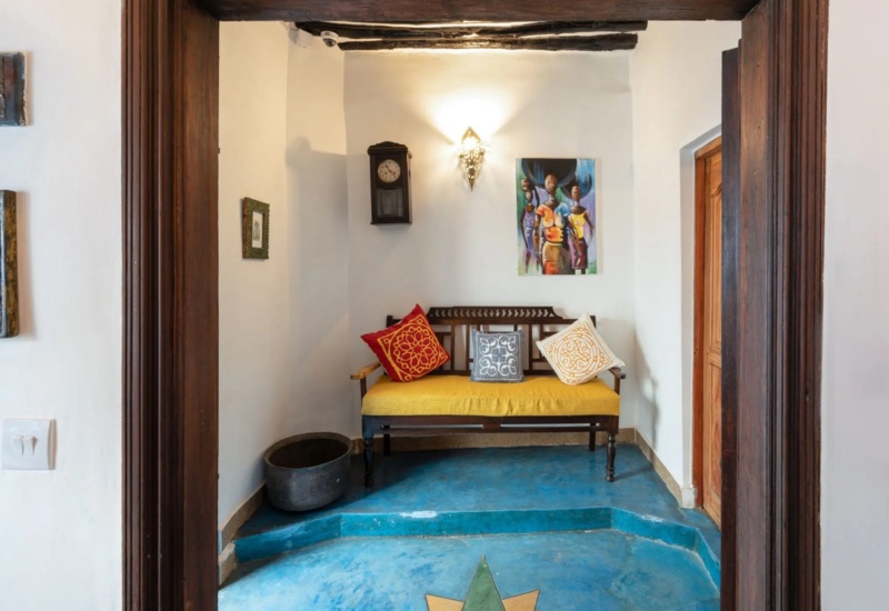 Cozy hotel seating area with wooden bench, colorful patterned cushions, vintage wall clock, and vibrant floor with star design.