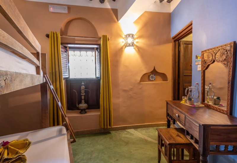 Cozy room with wooden bunk beds, carved dressing table, yellow curtains, warm wall sconce, and rustic open window detailing.