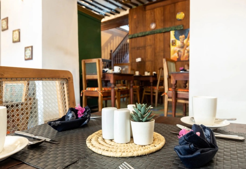 Cozy restaurant table with wooden chairs, cups on white saucers, folded napkins with flowers, and a small potted succulent centerpiece