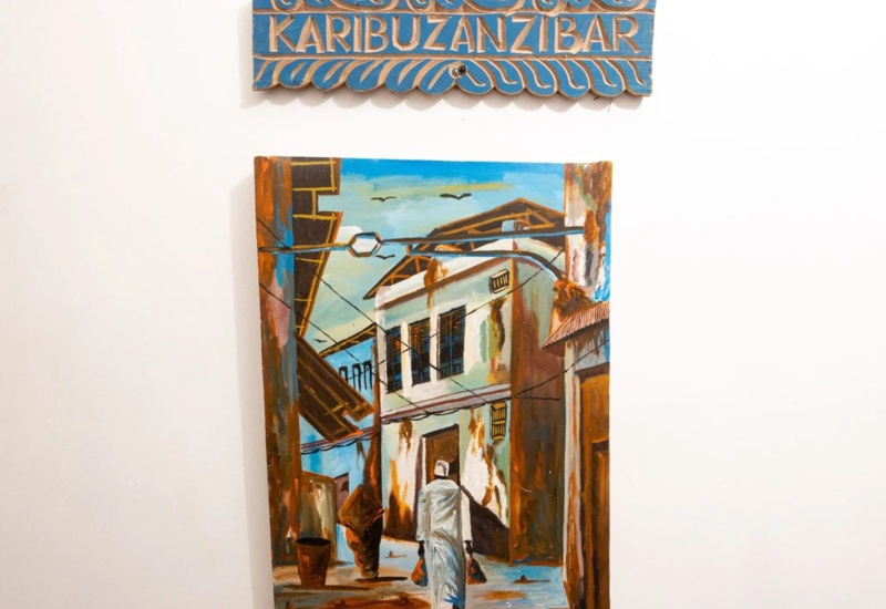 Colorful painting of a narrow street in Zanzibar with traditional buildings and a person walking away carrying bags