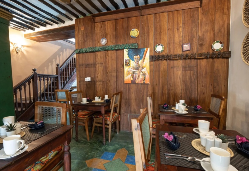 Cozy dining area with wooden tables and chairs, colorful cushions, tribal wall art, woven baskets, and warm ambient lighting