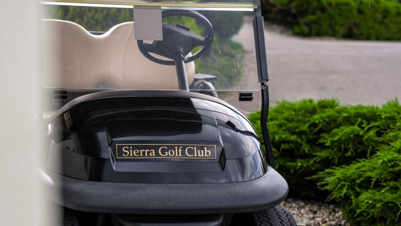 Wózek golfowy Sierra Golf Club z beżowym siedzeniem i daszkiem, zaparkowany przy ścieżce obok zieleni i namiotów.