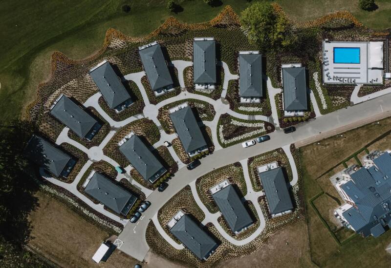 Widok z lotu ptaka na kompleks willi z prywatnymi tarasami, uporządkowanymi ścieżkami, parkingami i odkrytym basenem przy polu golfowym.