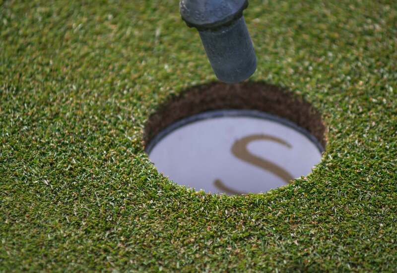 Zielony putting green hotelowego pola golfowego, otwarty dołek z widoczną wkładką i podniesionym masztkiem