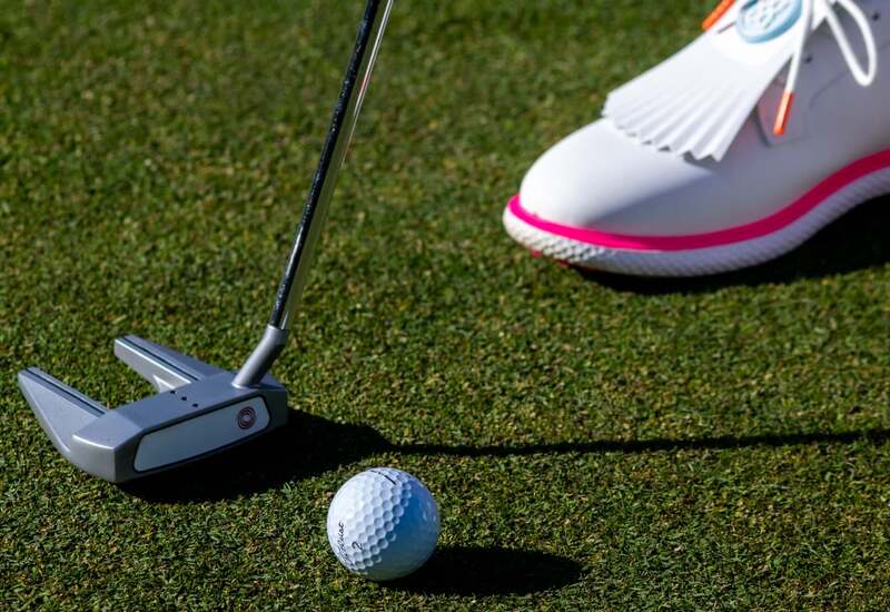 Putter i piłka na zadbanym greenie hotelowego pola golfowego, biały but z różową lamówką przy piłce