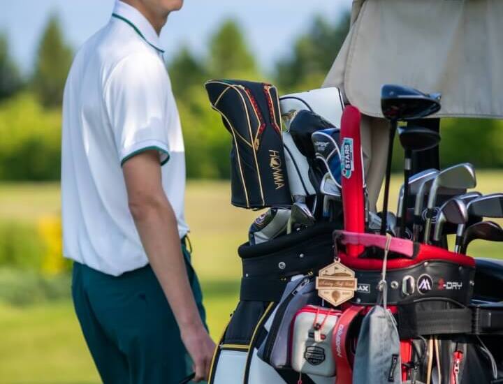 Młody golfista stoi przy torbie z kijami na wózku golfowym na zielonym polu golfowym