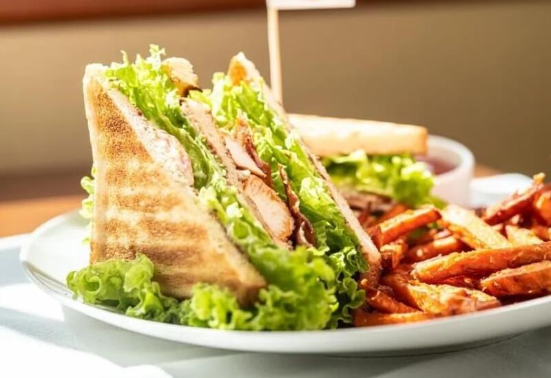 Club sandwich z grillowanym pieczywem, sałatą i kurczakiem, ozdobiony chorągiewką, podany z batatowymi frytkami i sosem