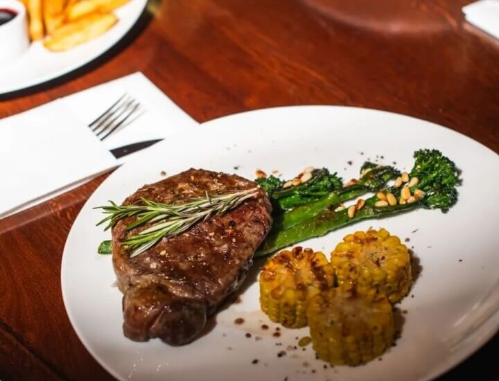 Stek z rozmarynem na talerzu z grillowaną kukurydzą i brokułami, restauracyjne danie serwowane przy drewnianym stole.