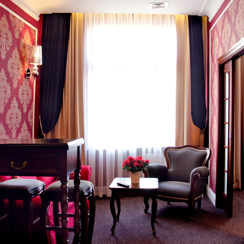 Sitting area with an armchair, side table, desk and large window in Junior Suite Deluxe Red