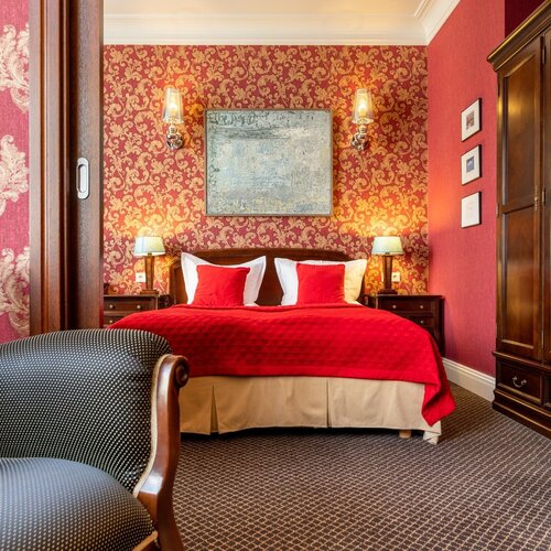 Full view of the bedroom with a double bed, red bedspread, armchair and wardrobe in Junior Suite Deluxe Red
