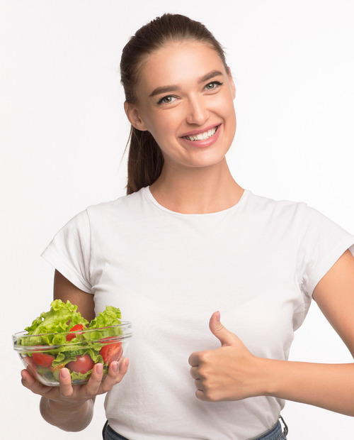 Uśmiechnięta kobieta trzyma miskę sałatki i pokazuje kciuk w górę, promując zdrowe posiłki.