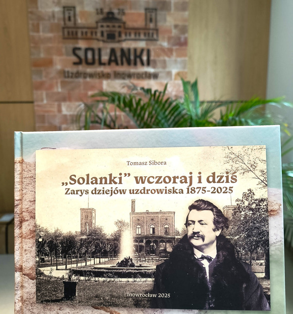 Book 'Solanki' 1875–2025 on a spa lobby stand, historic cover with a portrait and fountain, hotel logo visible behind