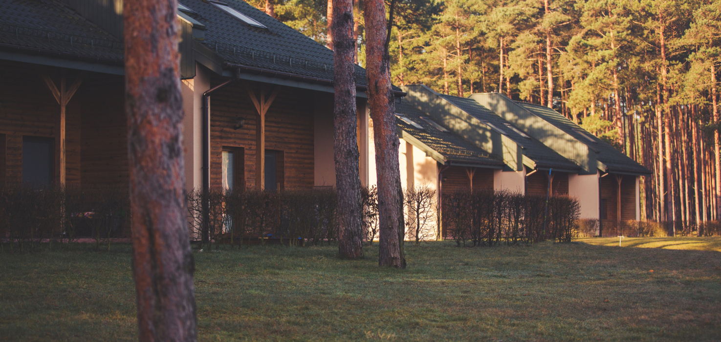 Szereg przytulnych apartamentów całorocznych z ciemnymi dachami w otoczeniu sosnowego lasu i zielonego trawnika przy zachodzie słońca.