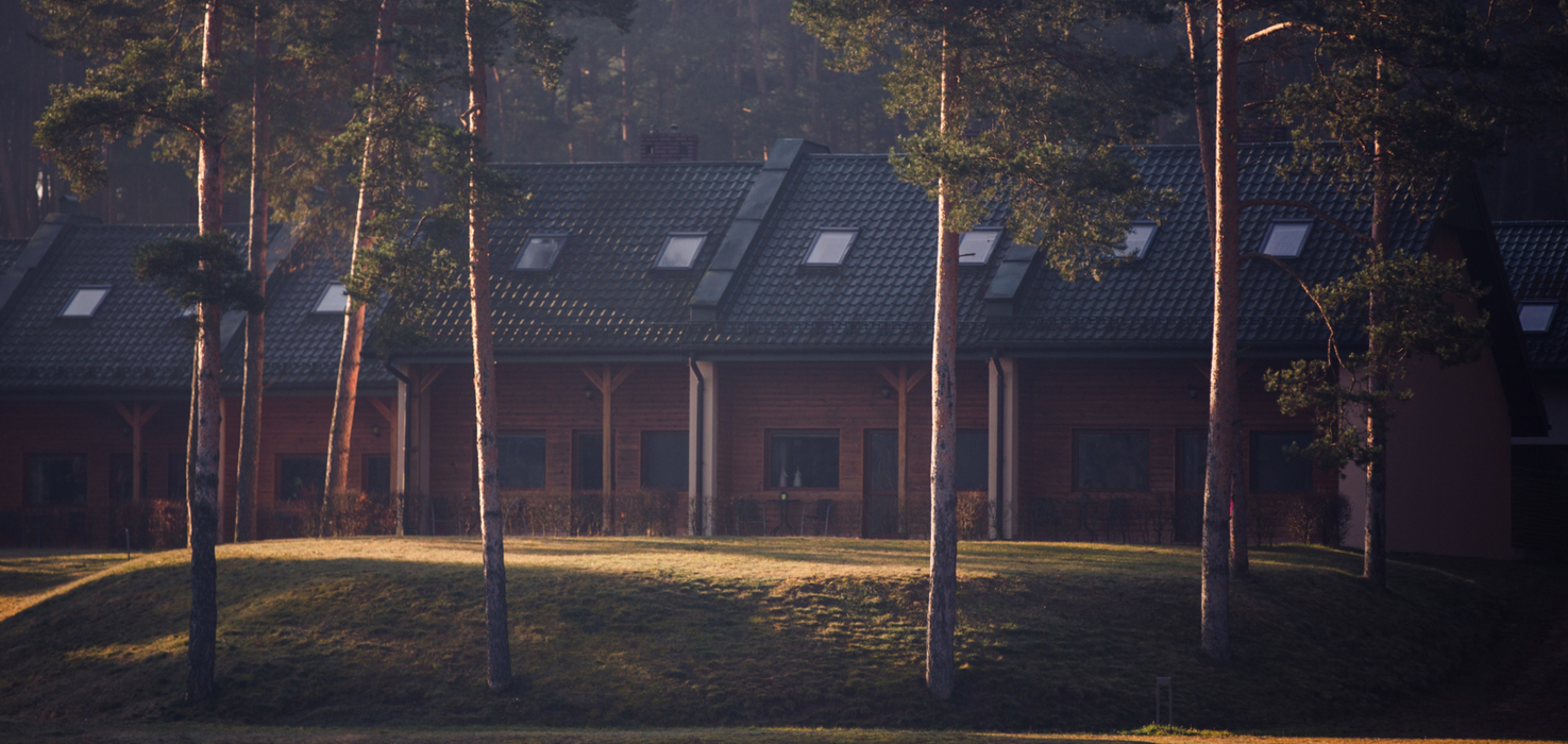 Apartamenty całoroczne z ciemnym dachem i poddaszem, otoczone sosnowym lasem w miękkim świetle poranka.