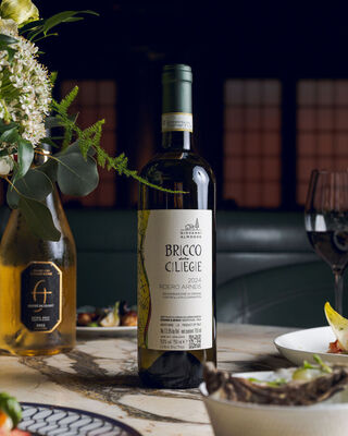 Bottled Italian Roero Arneis on marble table with floral arrangement, plated dishes and a wine glass in a refined restaurant.