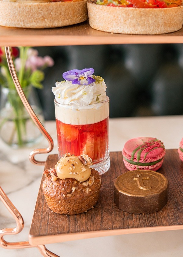 Copper stand of afternoon-tea treats: strawberry parfaits with cream and flowers, pink macarons, gold bonbons, caramel cakes