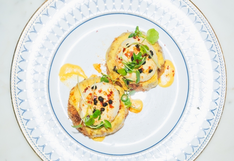 Two poached eggs with hollandaise and microgreens on toasted rounds, served on patterned porcelain plate over marble