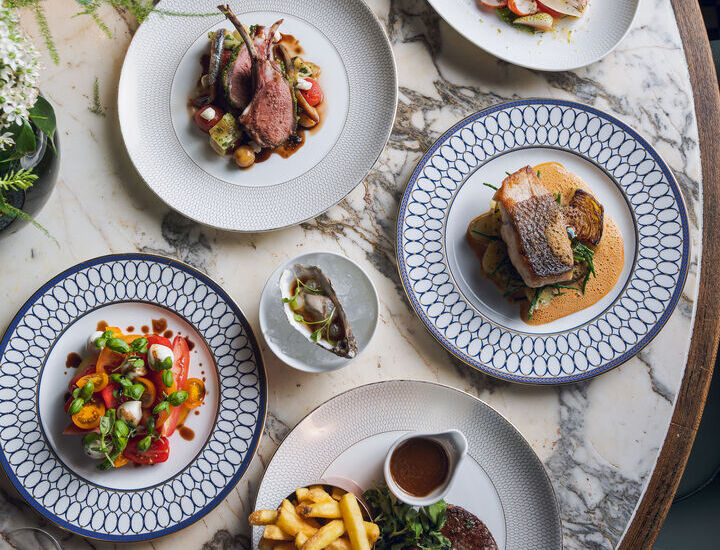 Elegant marble-top table set with chef-crafted dishes: lamb chops, seared fish, steak with fries and sauce, fresh salads, oyster and glass of red wine.