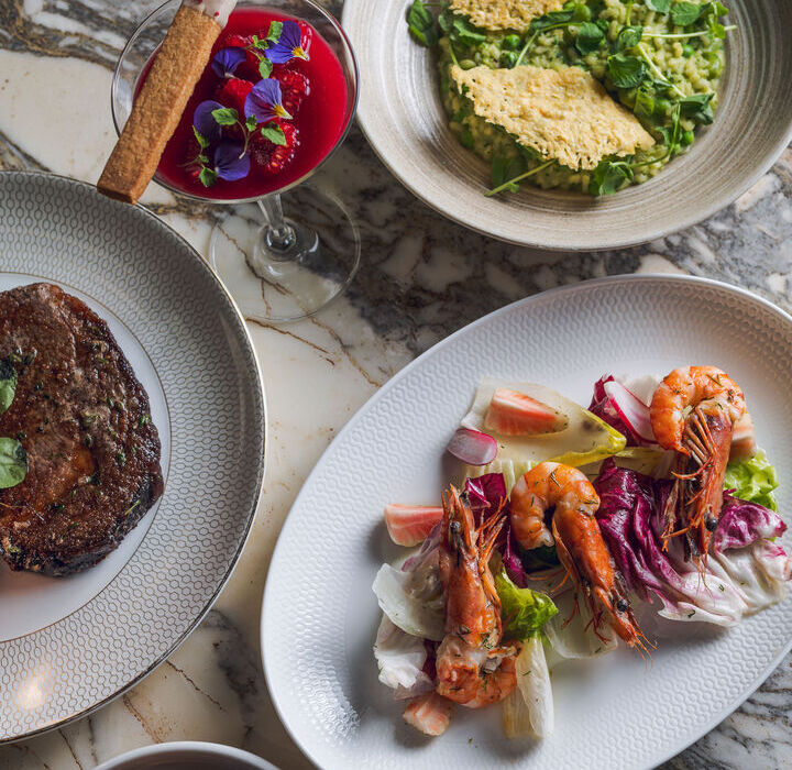 Gourmet surf-and-turf on marble: prawn salad, green risotto with parmesan crisps, grilled steak, pastries and a red floral cocktail.