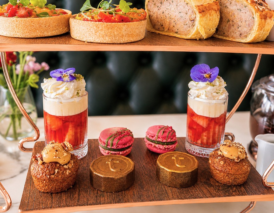 Two-tier copper tea stand with fruit tarts and savory roll; strawberry parfaits topped with cream, pink macarons and gold chocolate domes.