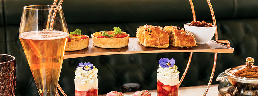 Elegant afternoon tea with tiered stand of savory tarts and pastries, petite desserts, sparkling wine and teapot on table.
