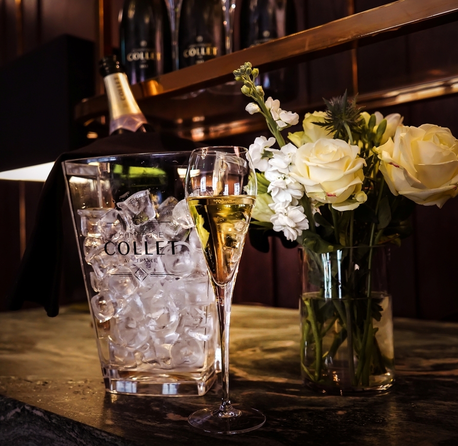 Chilled champagne in an ice bucket, filled flute of sparkling wine and white rose bouquet on an elegant hotel bar.