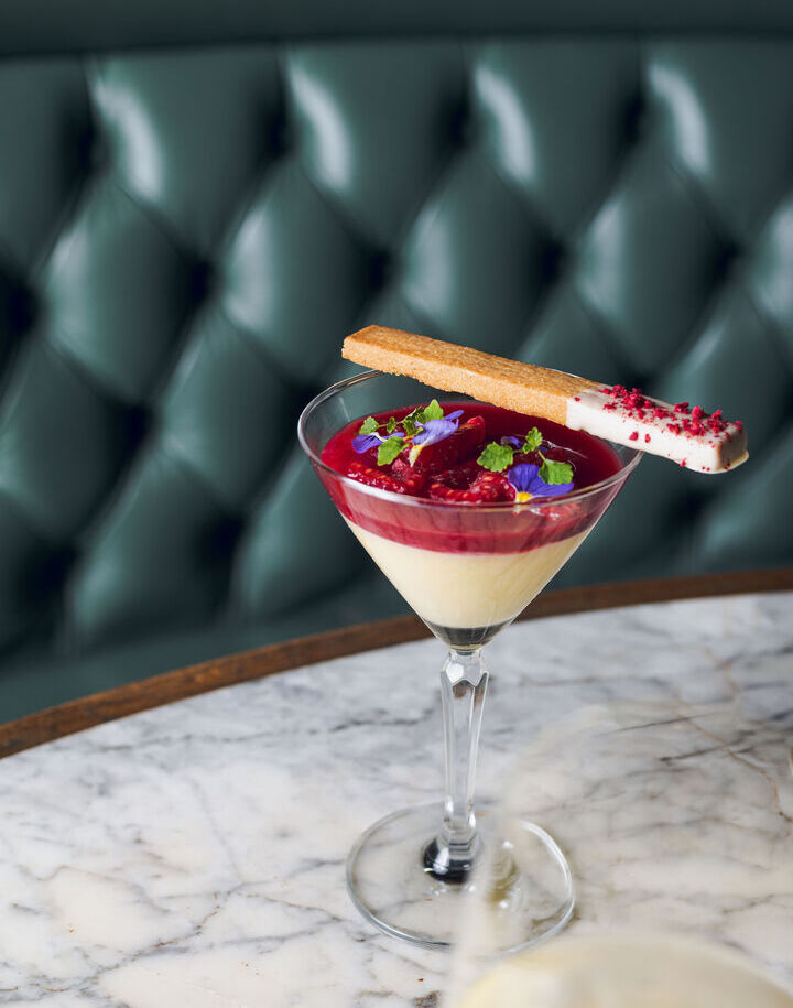 Vanilla panna cotta with raspberry coulis, fresh raspberries and edible flowers, topped with a white-chocolate-dipped biscuit.