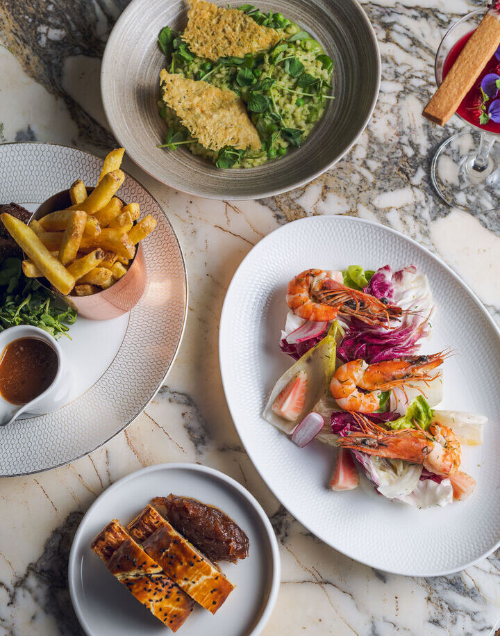 Gourmet spread on marble table: prawn salad with radicchio and citrus, fries with dipping sauce, pea risotto with parmesan crisps and sesame pastry.