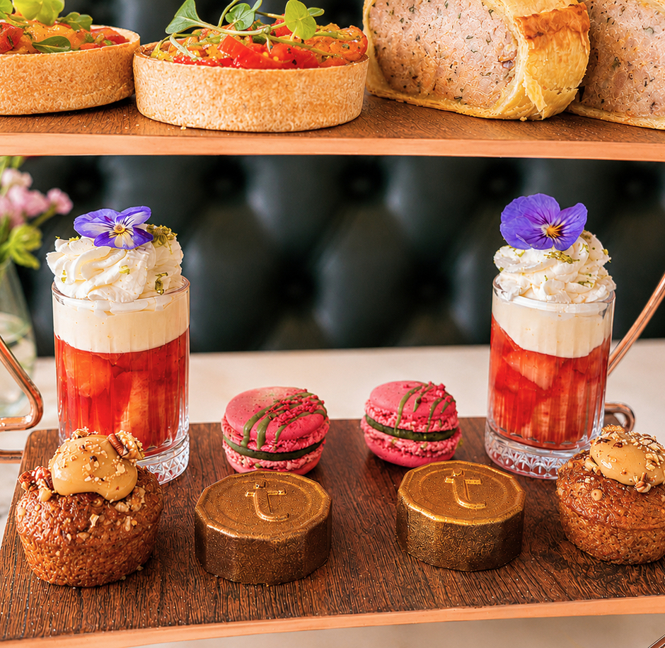 Two-tier copper tea stand with fruit tarts and savory roll; strawberry parfaits topped with cream, pink macarons and gold chocolate domes.