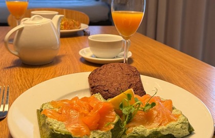In-room breakfast: smoked salmon on spinach toast with herb cream, chocolate cookie, orange juice and tea in a cozy hotel room.