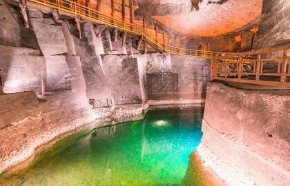 Underground salt chamber with illuminated emerald pool, wooden visitor walkway and carved rock walls lit in warm tones