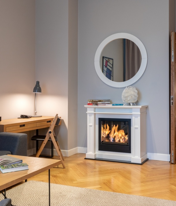 Przytulny apartament z działającym kominkiem, szarą sofą z czerwoną poduszką, drewnianym biurkiem, stołem i sypialnią z żółtymi poduszkami.