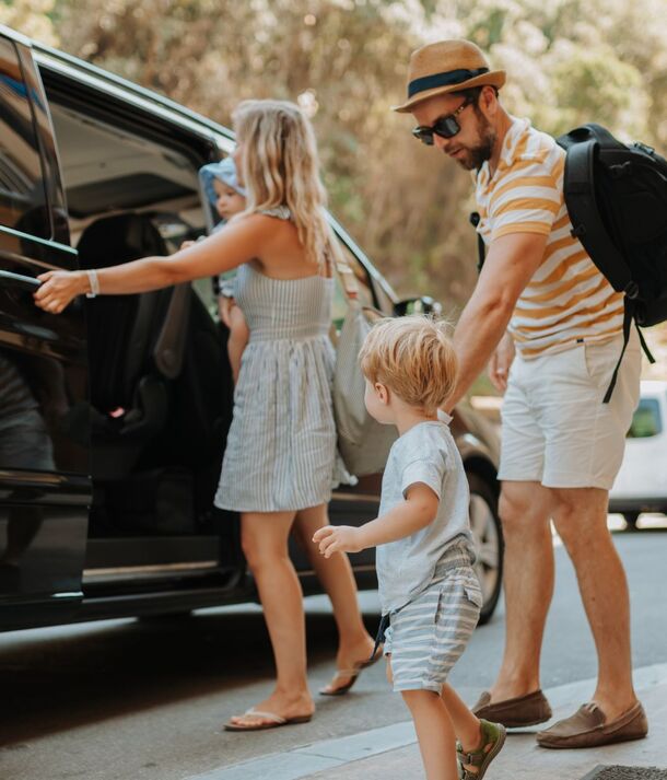 Rodzina wsiada do czarnego vana w słoneczny dzień, rodzice pomagają dwóm małym dzieciom wejść do auta