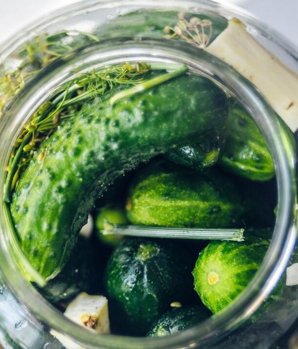 Szklany słoik jasnych zielonych korniszonów z koperkiem i czosnkiem, chrupiące miniogórki w zalewie — dodatek do dań