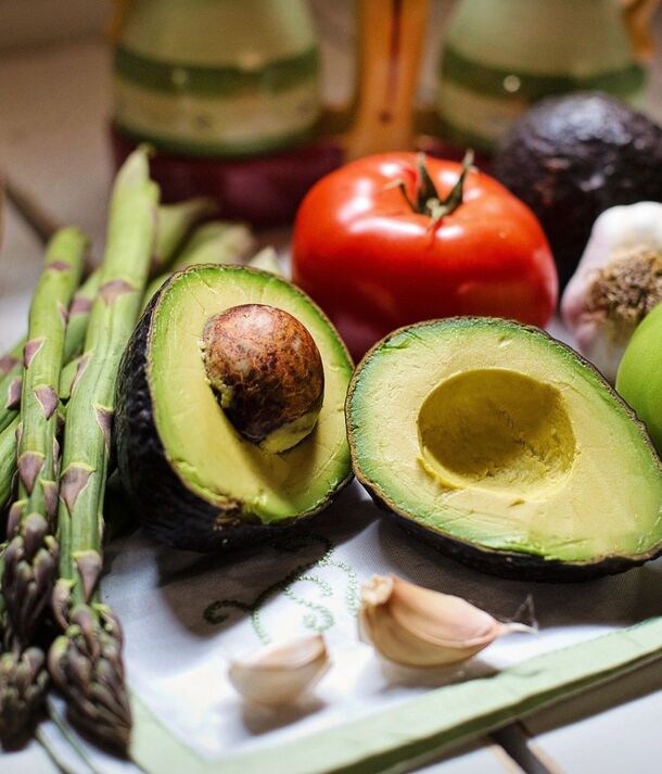 Dojrzałe awokado przecięte na pół z szparagami, pomidorem i czosnkiem na ściereczce — świeże składniki na śniadanie