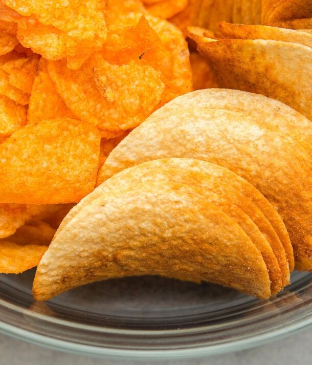 Szklana miska z przyprawionymi, falistymi chipsami oraz ułożonymi cienkimi, zakrzywionymi chipsami ziemniaczanymi