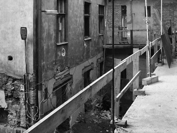 Wąska kładka rusztowania nad podwórzem starego hotelu w remoncie, odsłonięte ceglane ściany, poręcze i pracownik.