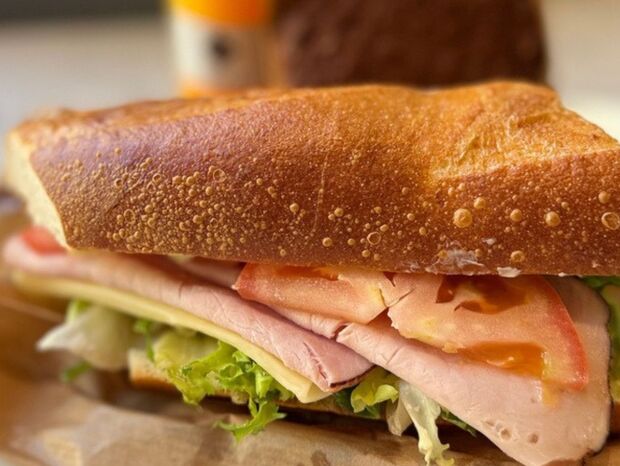 Bagietka z szynką, serem, świeżą sałatą i plastrami pomidora na papierze