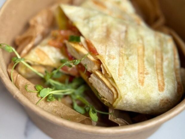 Grillowana tortilla z kurczakiem i warzywami, ozdobiona mikroliśćmi, podana w ekologicznym pojemniku na wynos.