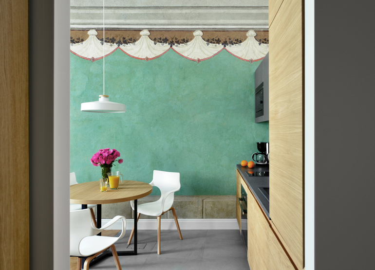 Kitchenette dining nook with round wood table, white chairs, turquoise fresco wall, pendant light, flowers, juice and coffee.