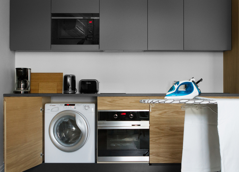 Compact kitchenette with built-in washing machine and oven, microwave, coffee maker, toaster, kettle and ironing board with iron