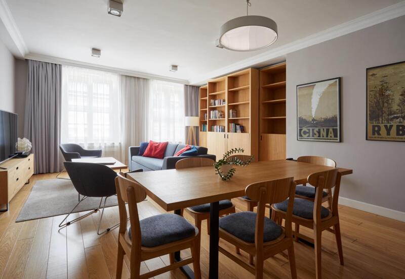 Przestronny nowoczesny apartament — salon z jadalnią: drewniany stół, 4 krzesła, szara sofa z czerwonymi poduszkami, fotele, regał i telewizor