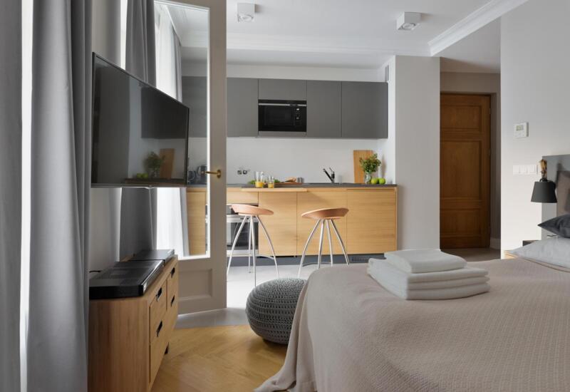 Studio z łóżkiem i złożonymi ręcznikami, aneksem kuchennym z hokerami, telewizorem na ścianie i stonowanym, przytulnym wystrojem